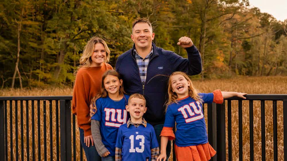 Joseph Escobar and his wife and three children standing on a wooden bridge with trees and a cornfield behind them.