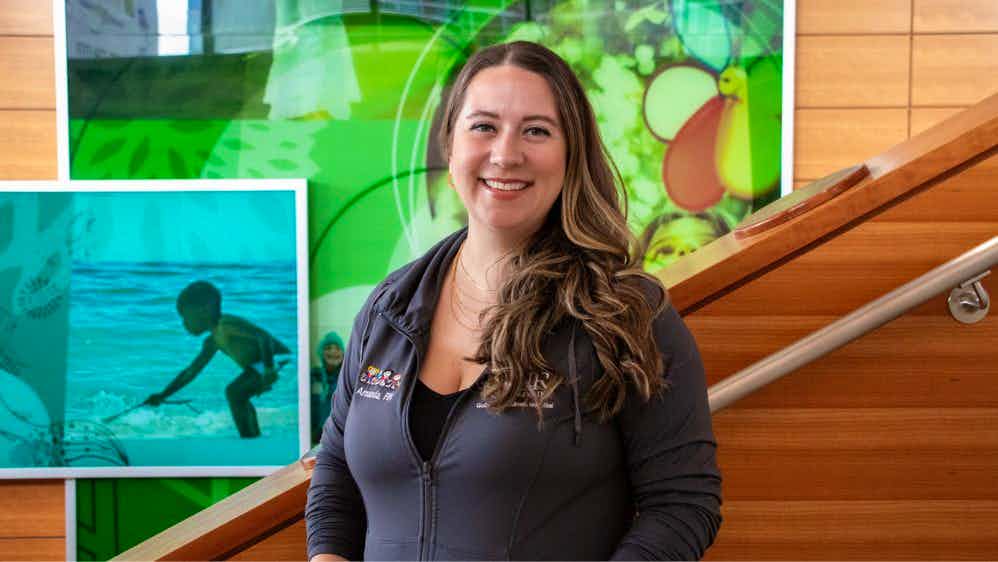 Photo of Amanda Welter on a staircase in the Children's Hospital, with a bright blue and green mural behind her.